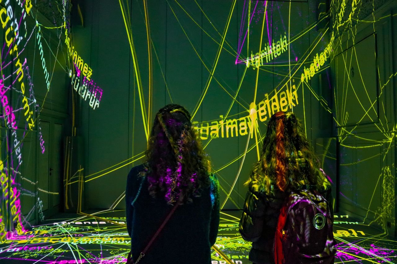 services-03 Two women observe a dynamic text projection art installation in a dark room.