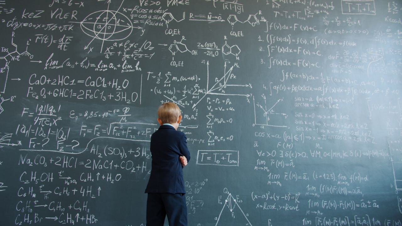 A child in a suit studies intricate mathematical equations on a chalkboard.