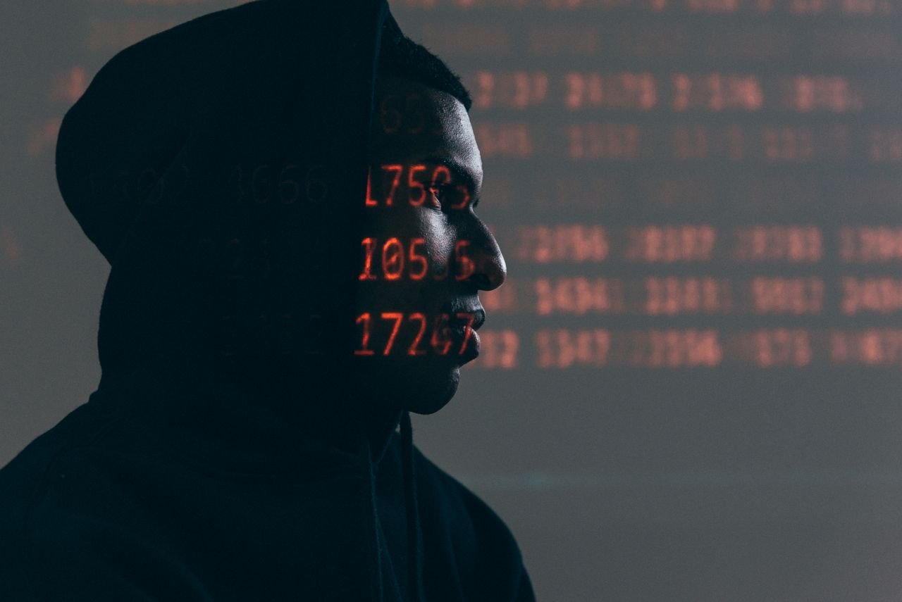 services-02 Side profile of a man in a hoodie, surrounded by red code, depicting cybersecurity theme.