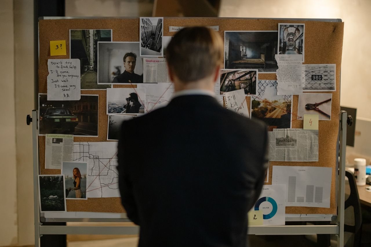 Detective examining clues on a bulletin board filled with photos and notes.